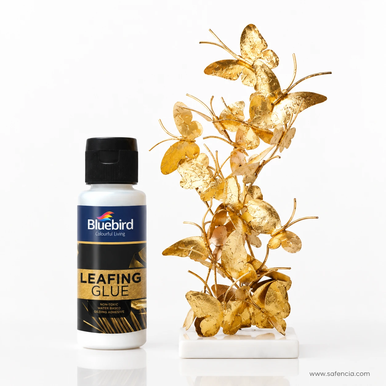 Bluebird Leafing Glue bottle standing beside intricate gilded golden butterfly branch sculpture on marble base