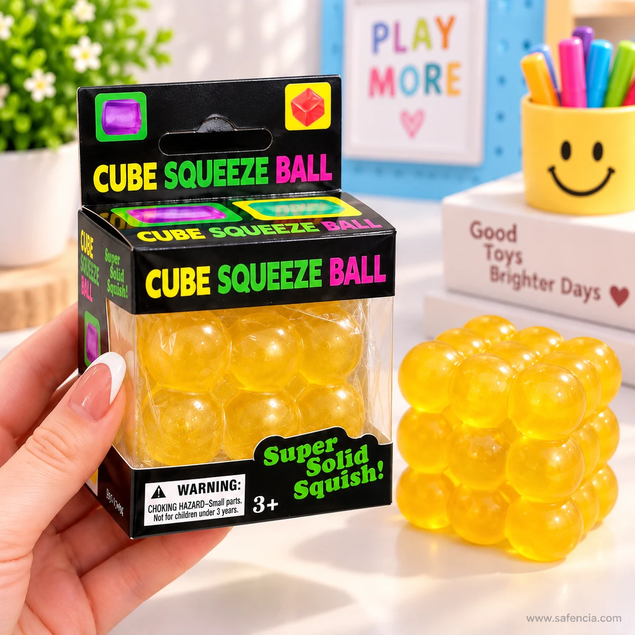 Hand holding a boxed yellow bubble squishy cube with a loose yellow cube beside it on a desk