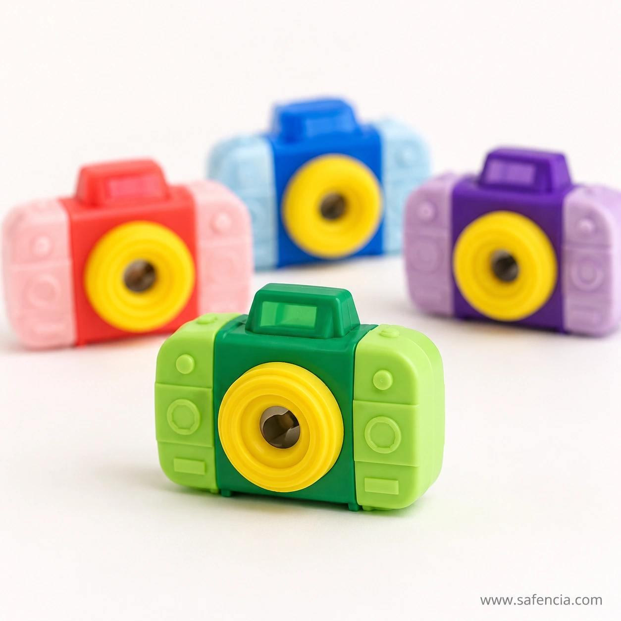 Green camera eraser sharpener in sharp focus showing the blade inside the yellow lens, with three other colours blurred behind