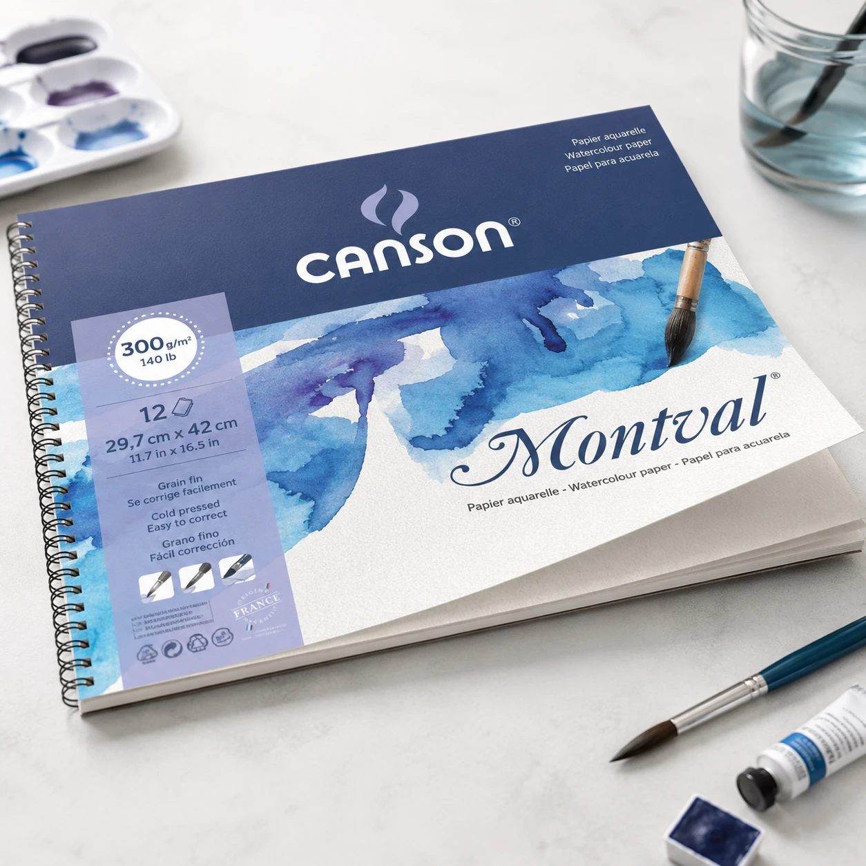 Canson Montval watercolor spiral pad on artist desk with paint tubes and palette