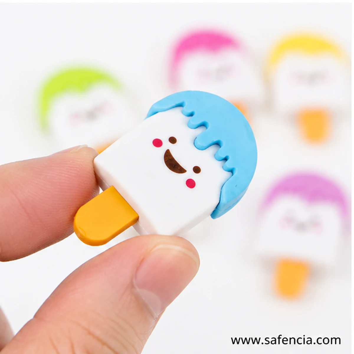 Blue-cap popsicle eraser held between a finger and thumb showing its small coin-like size, with more erasers blurred behind