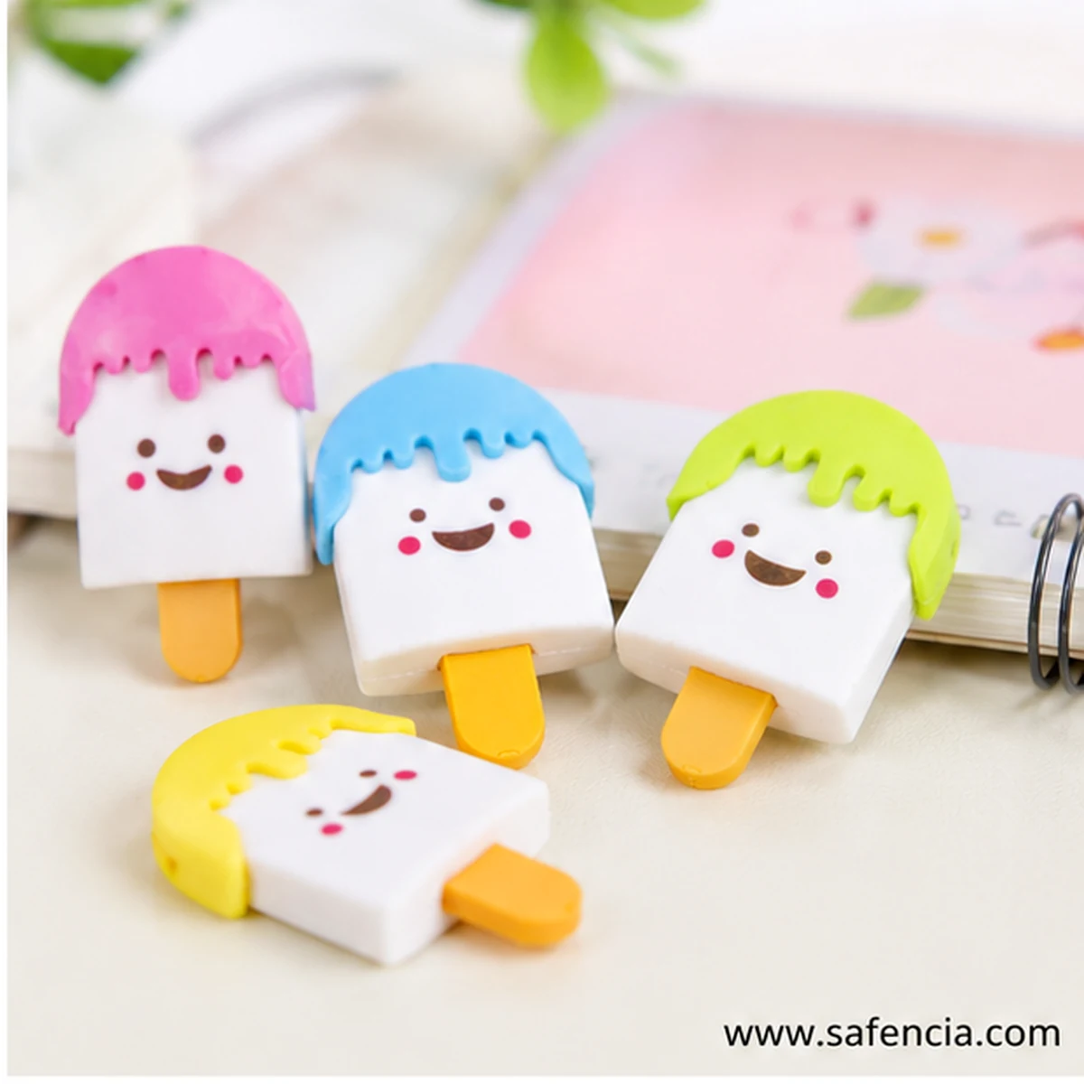 Four popsicle erasers in pink, blue, green and yellow leaning against a spiral notebook on a desk