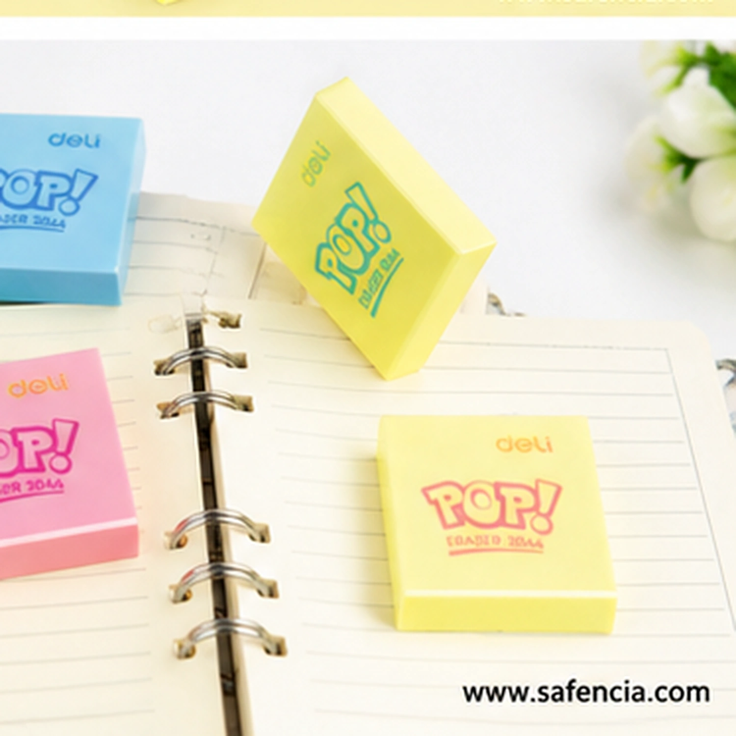 Deli Pop erasers in blue, pink and two yellows laid on an open ring bound notebook, one standing on edge to show the slim depth of the block