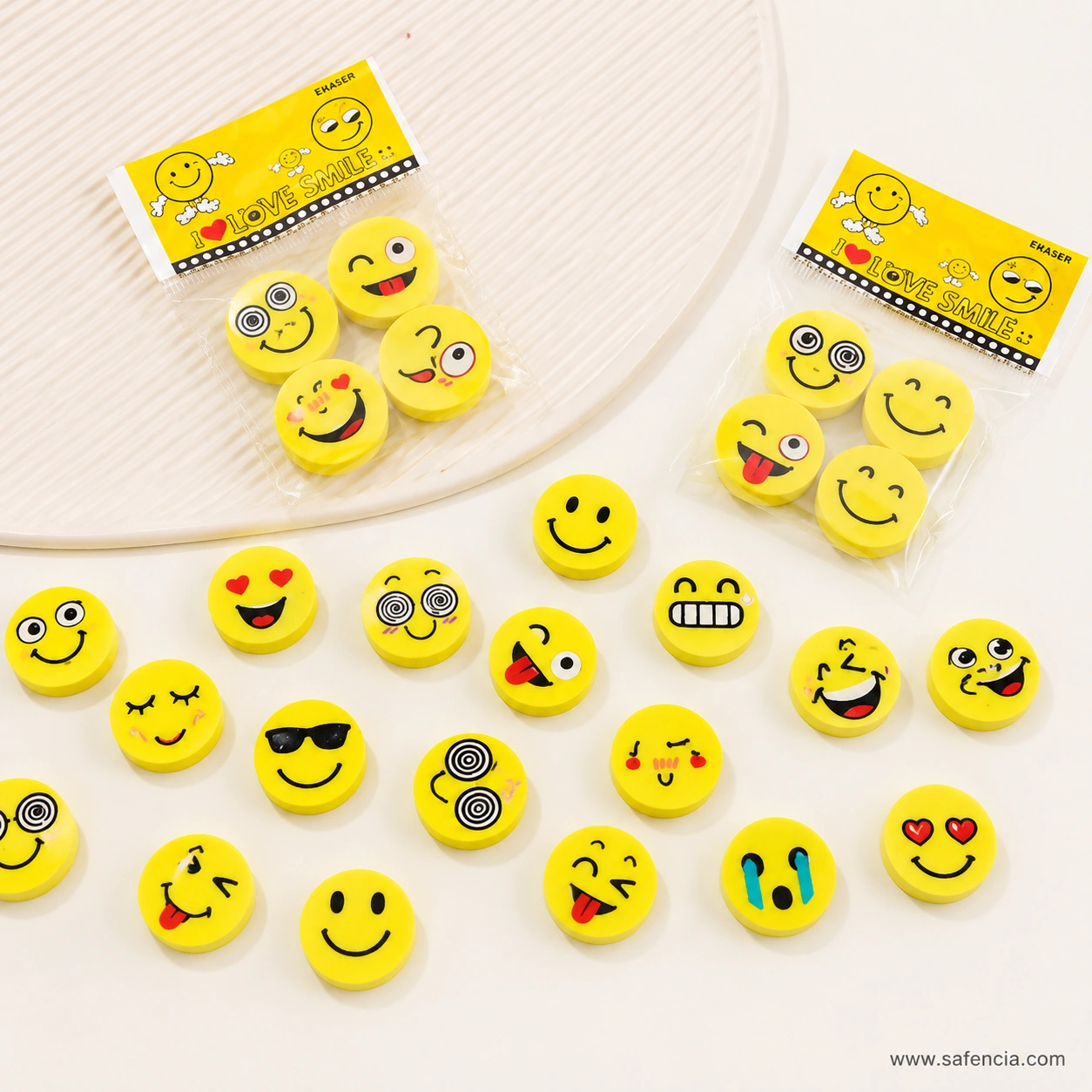 Two sealed emoji eraser bags with yellow header cards beside loose yellow face erasers spread on a pale surface