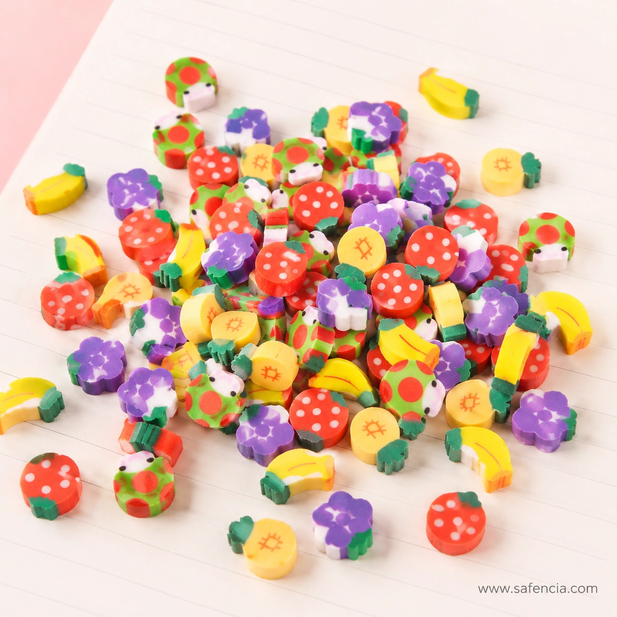 Miniature fruit-shaped erasers on ruled notebook paper including strawberries, grape bunches, bananas and pineapples