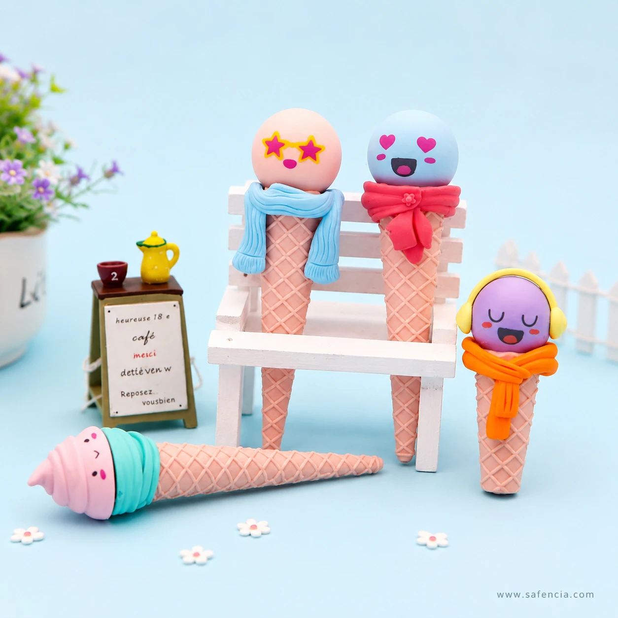 Funny face cone erasers arranged around a miniature white bench and cafe sign, with the soft-serve design lying in front