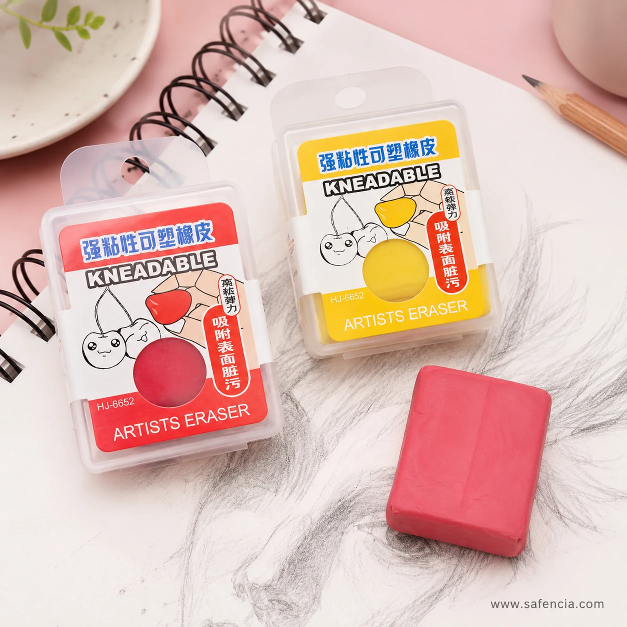 Red and yellow Kneadable Artists Eraser cases on a spiral sketchpad, with a pink kneadable block unwrapped and resting on a charcoal drawing