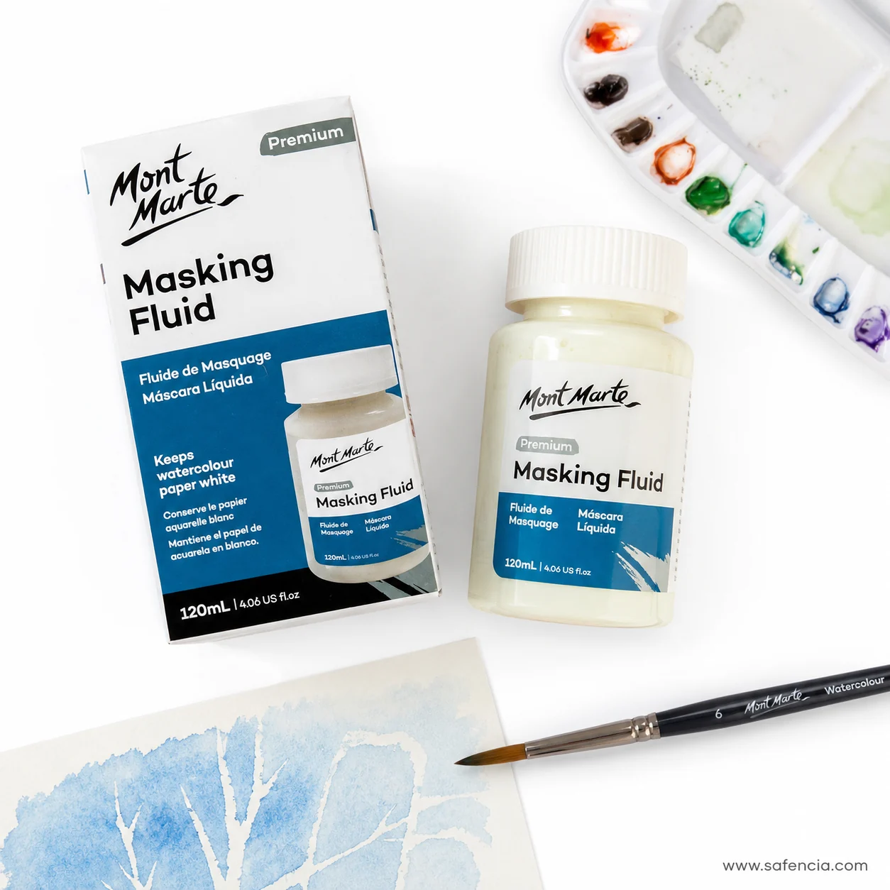Masking fluid jar and box beside a watercolour palette and a blue wash study with white branches