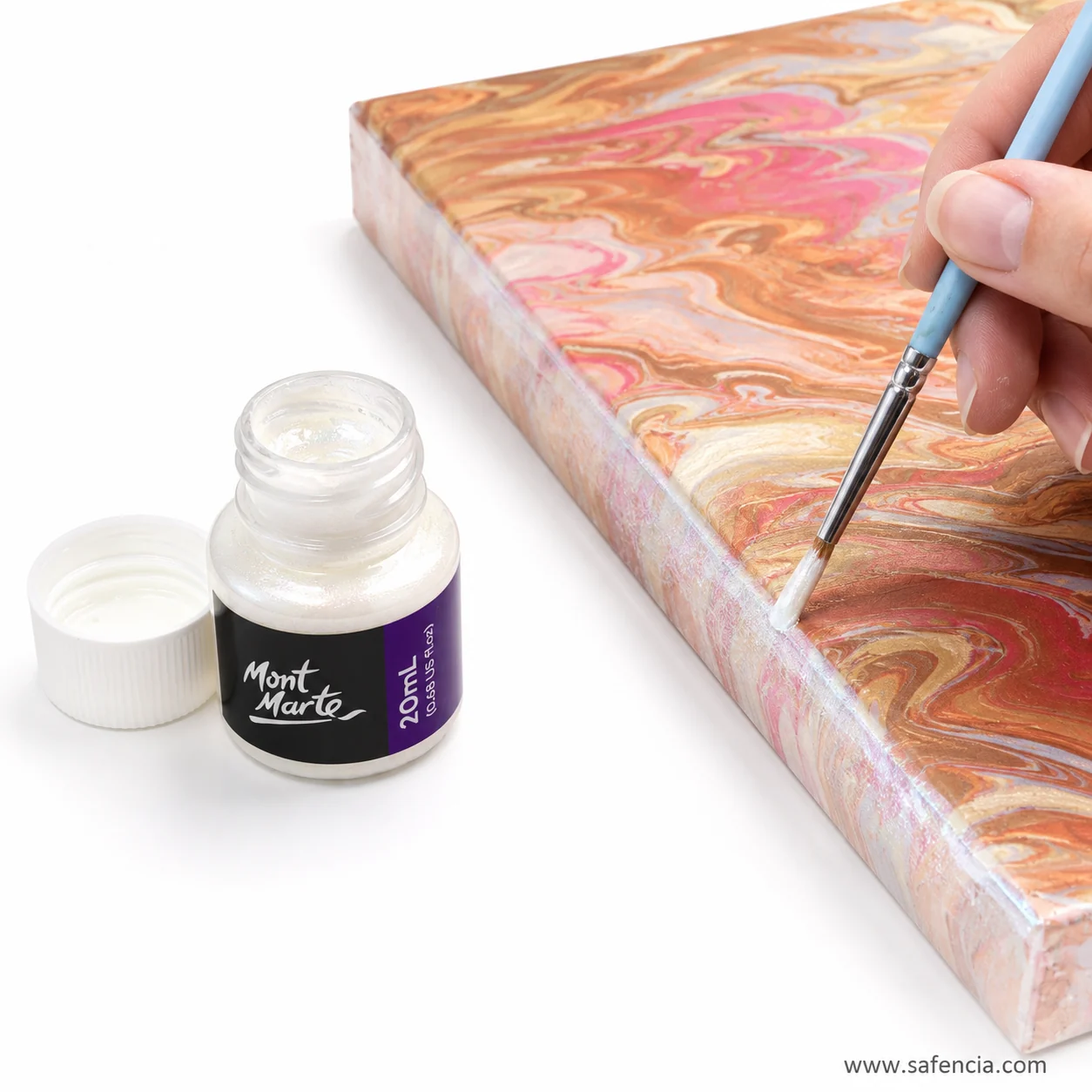 Iridescent foil paint being brushed onto a dry peach and rose acrylic pour canvas by hand