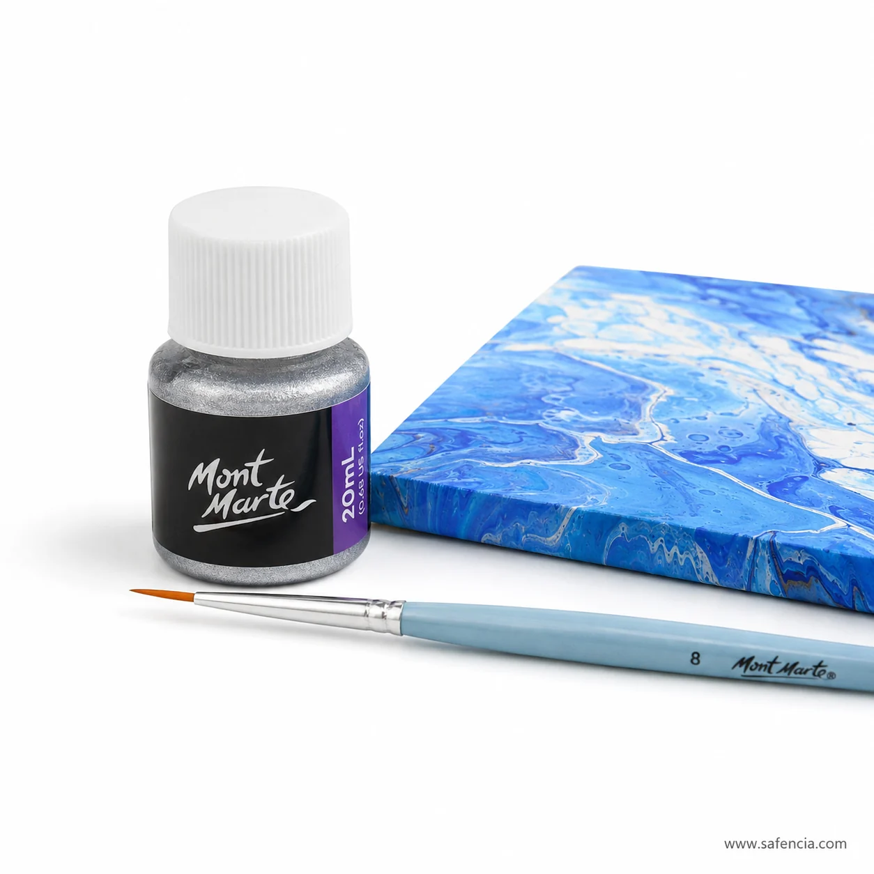 Silver foil paint bottle standing beside a finished blue and white acrylic pour canvas with a detail brush
