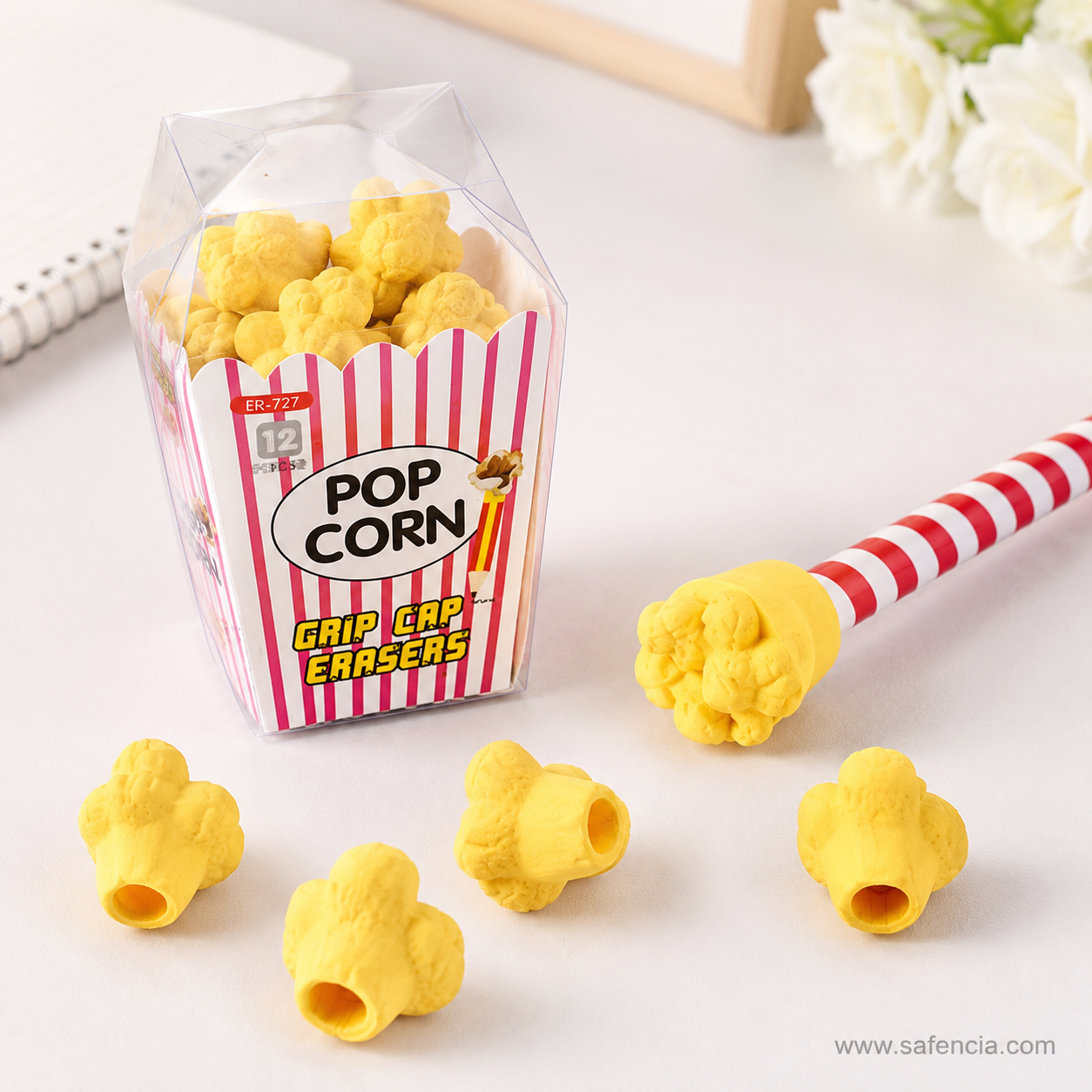 Popcorn cap eraser seated on the end of a red and white striped pencil beside the open popcorn box and loose kernels