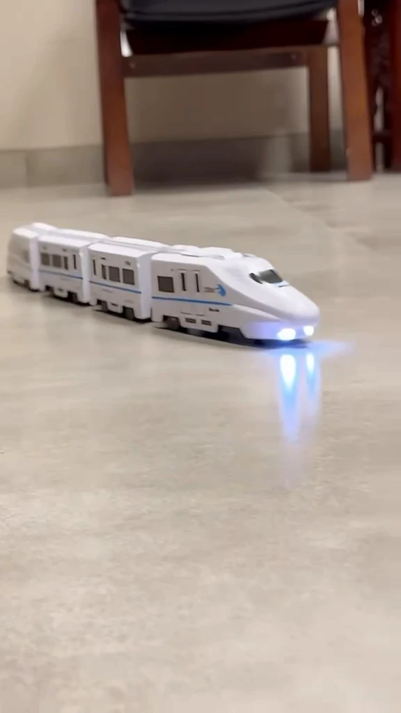 The four-car bullet train driving across a tiled floor at home with both headlights lit and reflecting